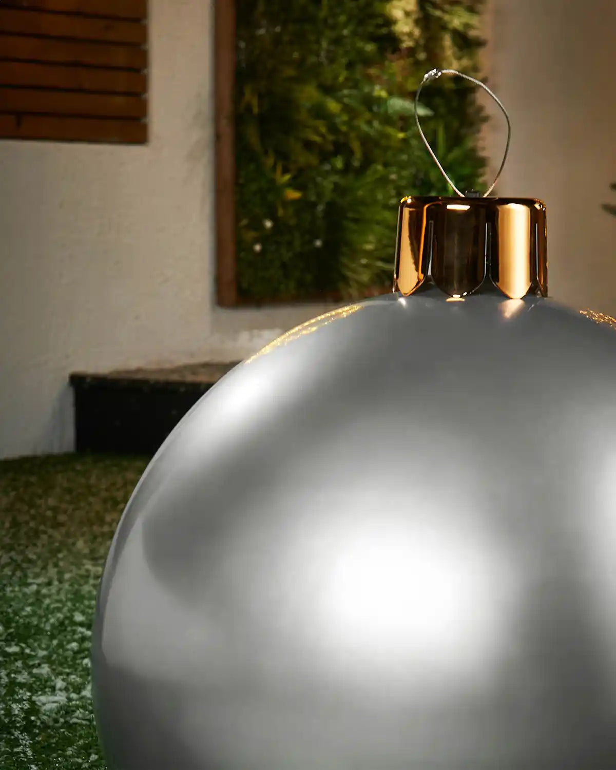 Close-up of a Medium silver Christmas inflatable bauble with gold cap against a blurred indoor background

