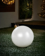Medium sized White inflatable bauble on a snowy garden floor with a decorated Christmas tree and wreath in background 
