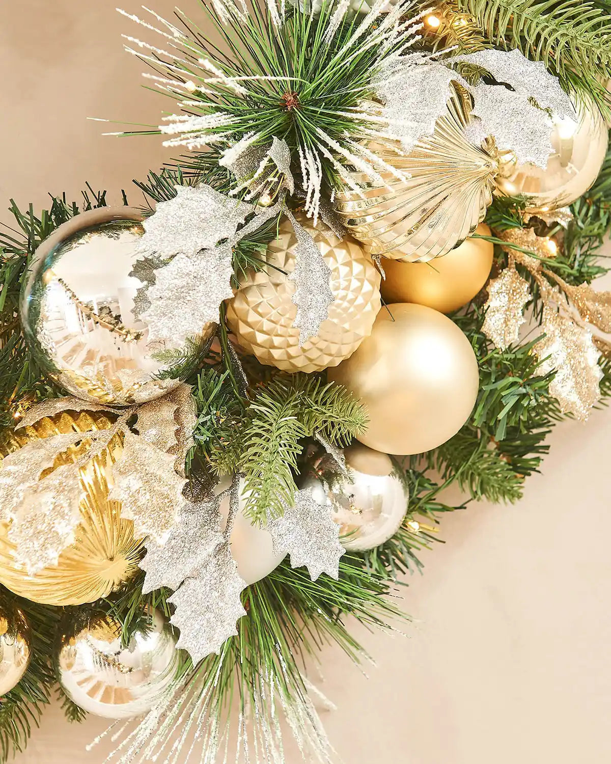 Close up of decorative wreath with gold, silver, and green ornaments on a beige background