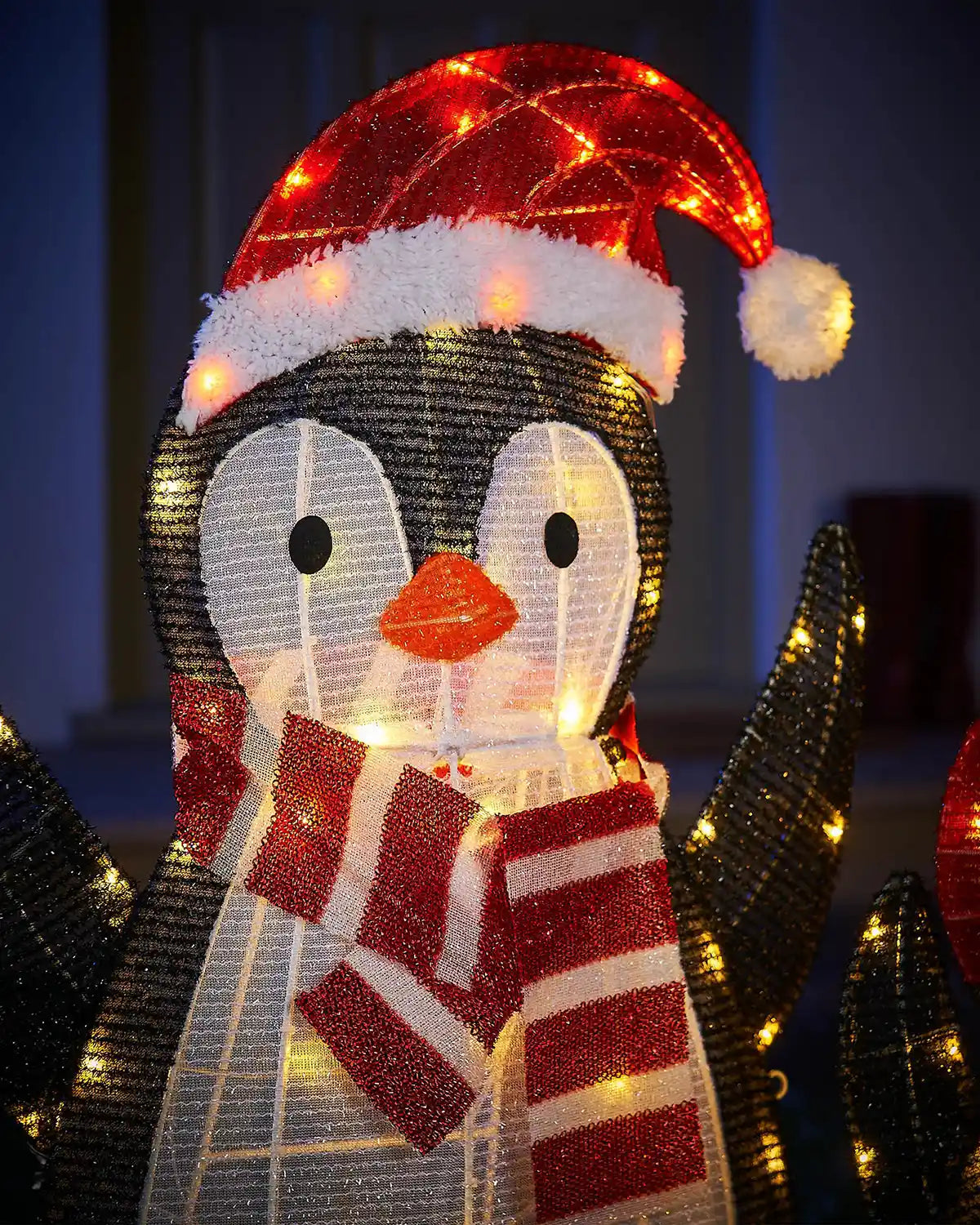 Decorative penguin figure wearing a Santa hat and scarf with lights on a dark background