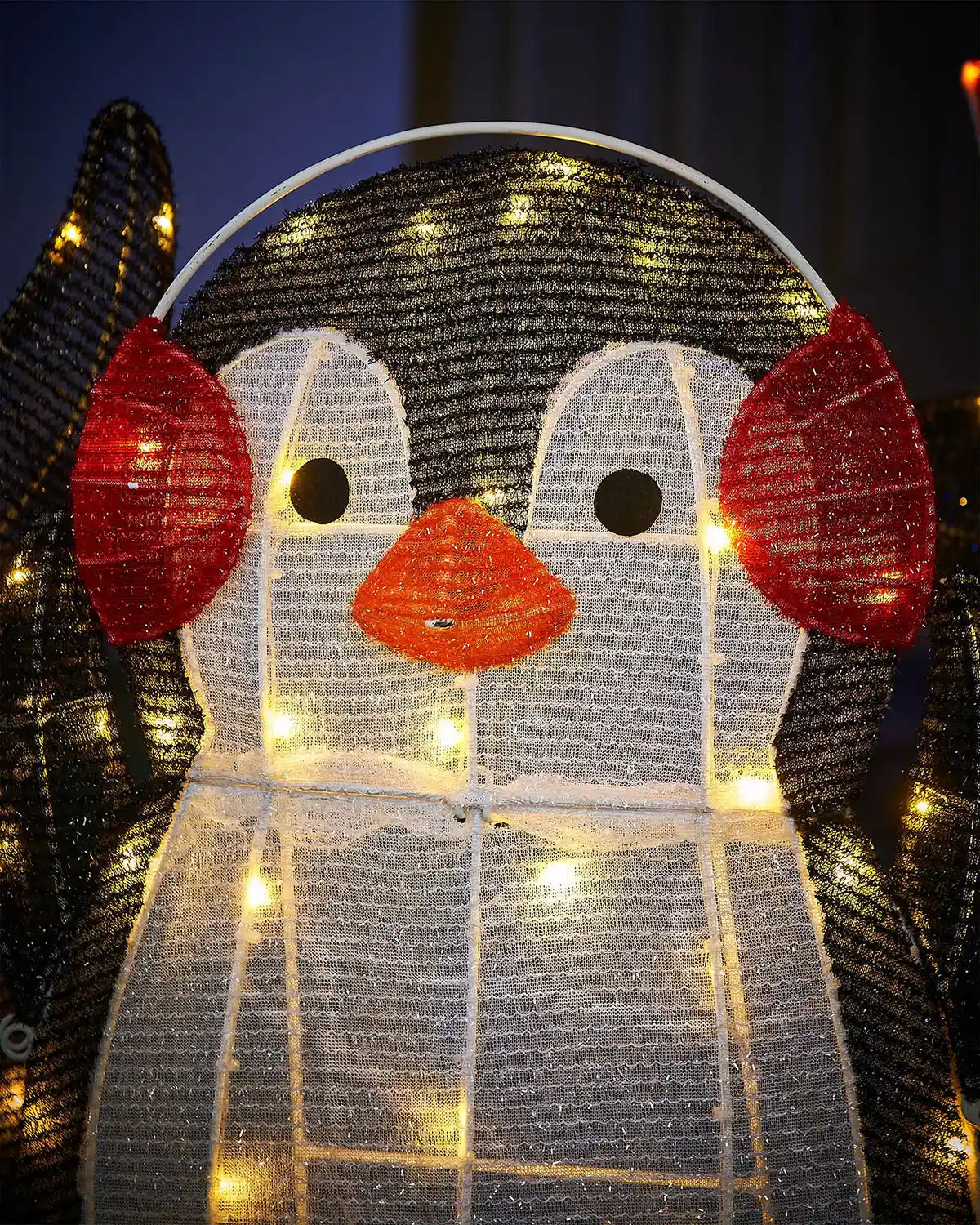 Decorative penguin light fixture wearing red ear muffs with glowing interior against a dark background