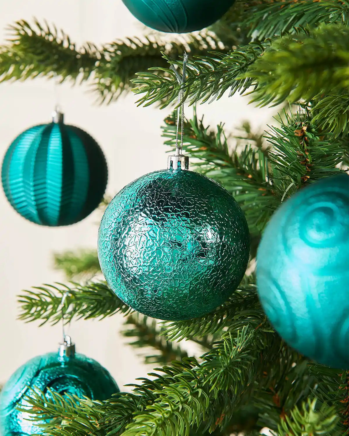 Turquoise Christmas ornaments on a tree branch with a light background