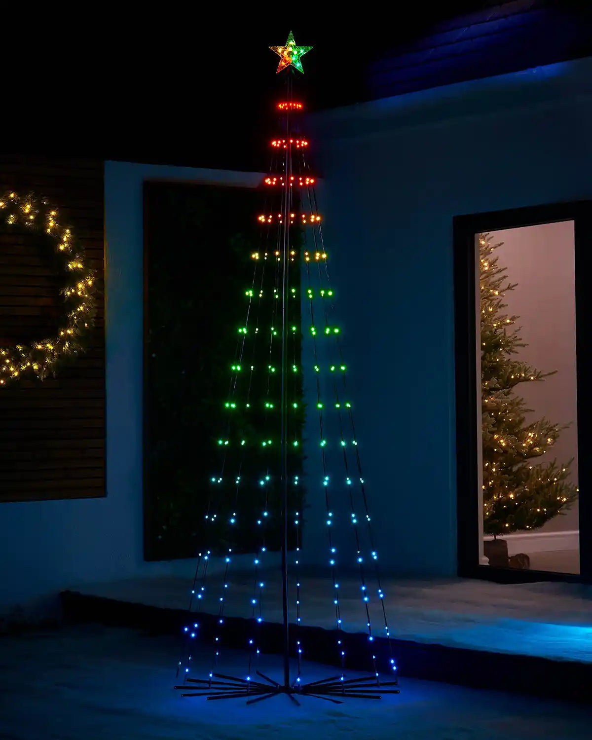 Decorative Multi-coloured LED string light tree on snowy grass and a decorated Christmas tree in background
