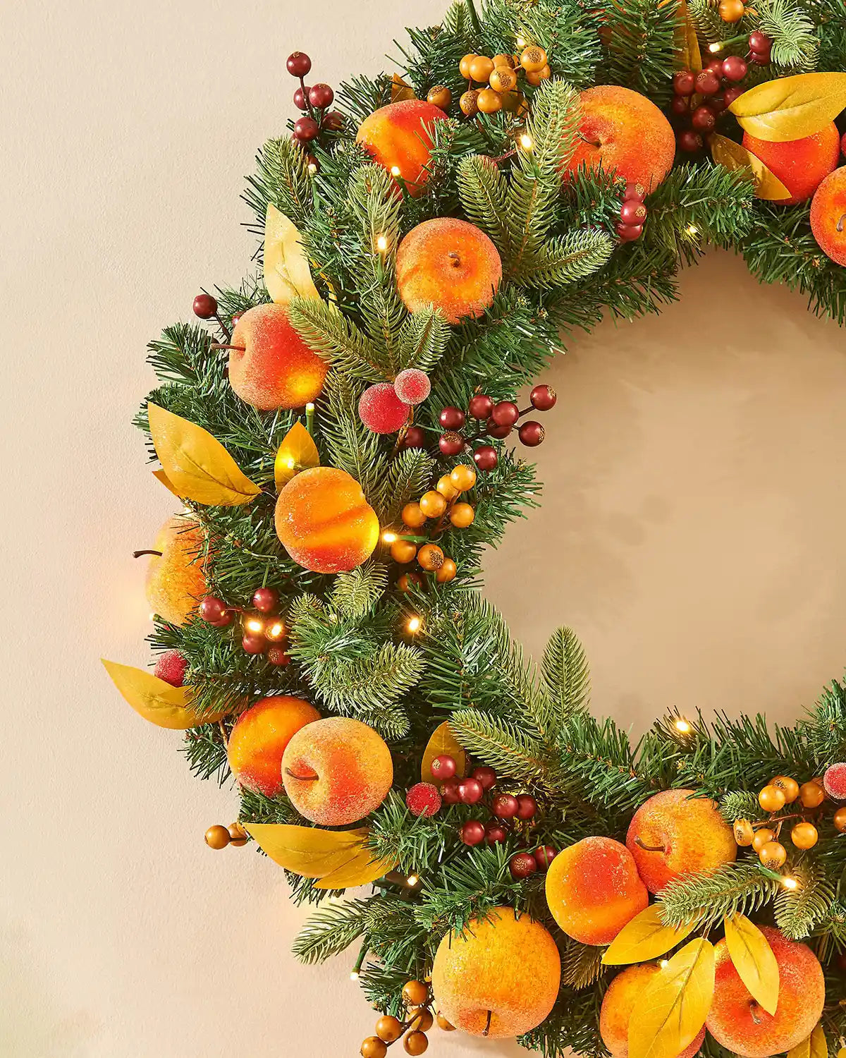 Side view of Artificial Oranges and peaches on a wreath against a cream background