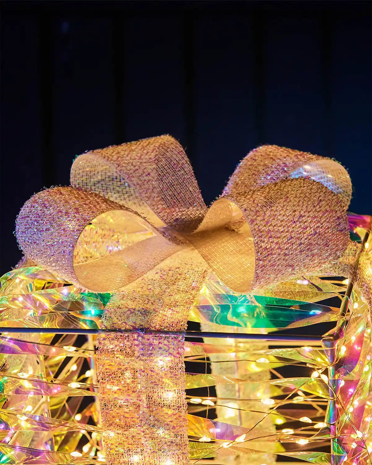 Light-up gift iridescent  box with LED lights and a white bow on a dark background.