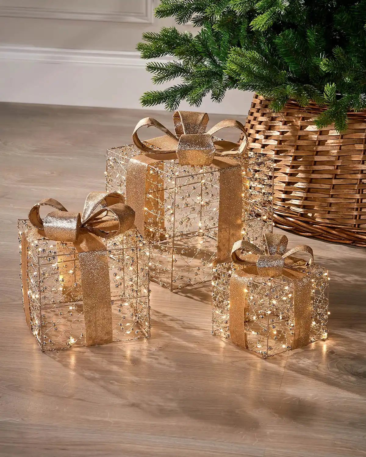 Decorative Christmas copper and gold presents boxes with gold ribbons on a wooden floor next to a Christmas tree.