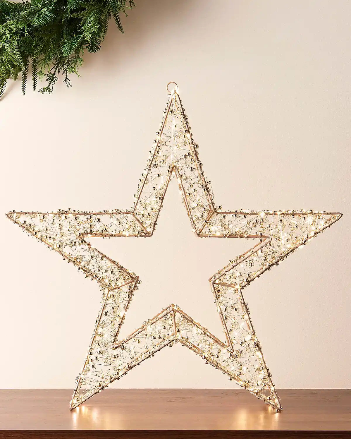 Gold star with gold beads warm white LED lights and copper wire on a wooden table