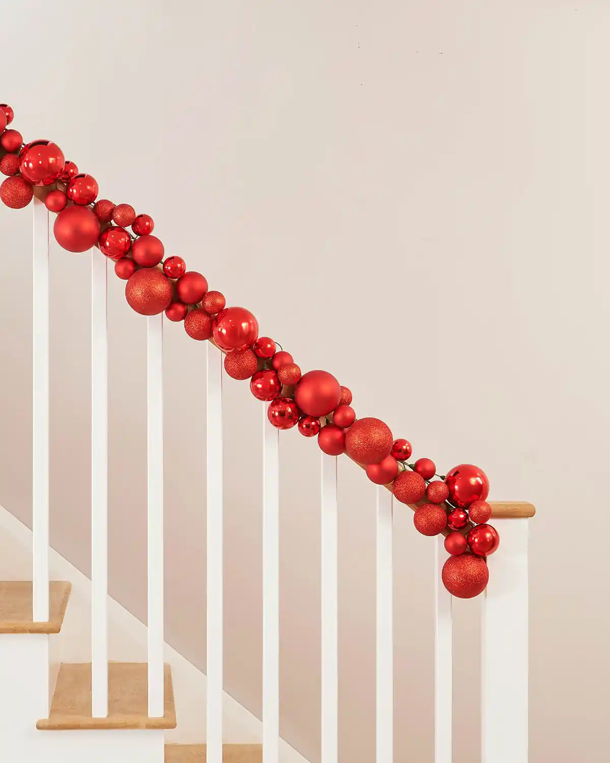 Red decorative bauble garland on a staircase railing against a beige wall.