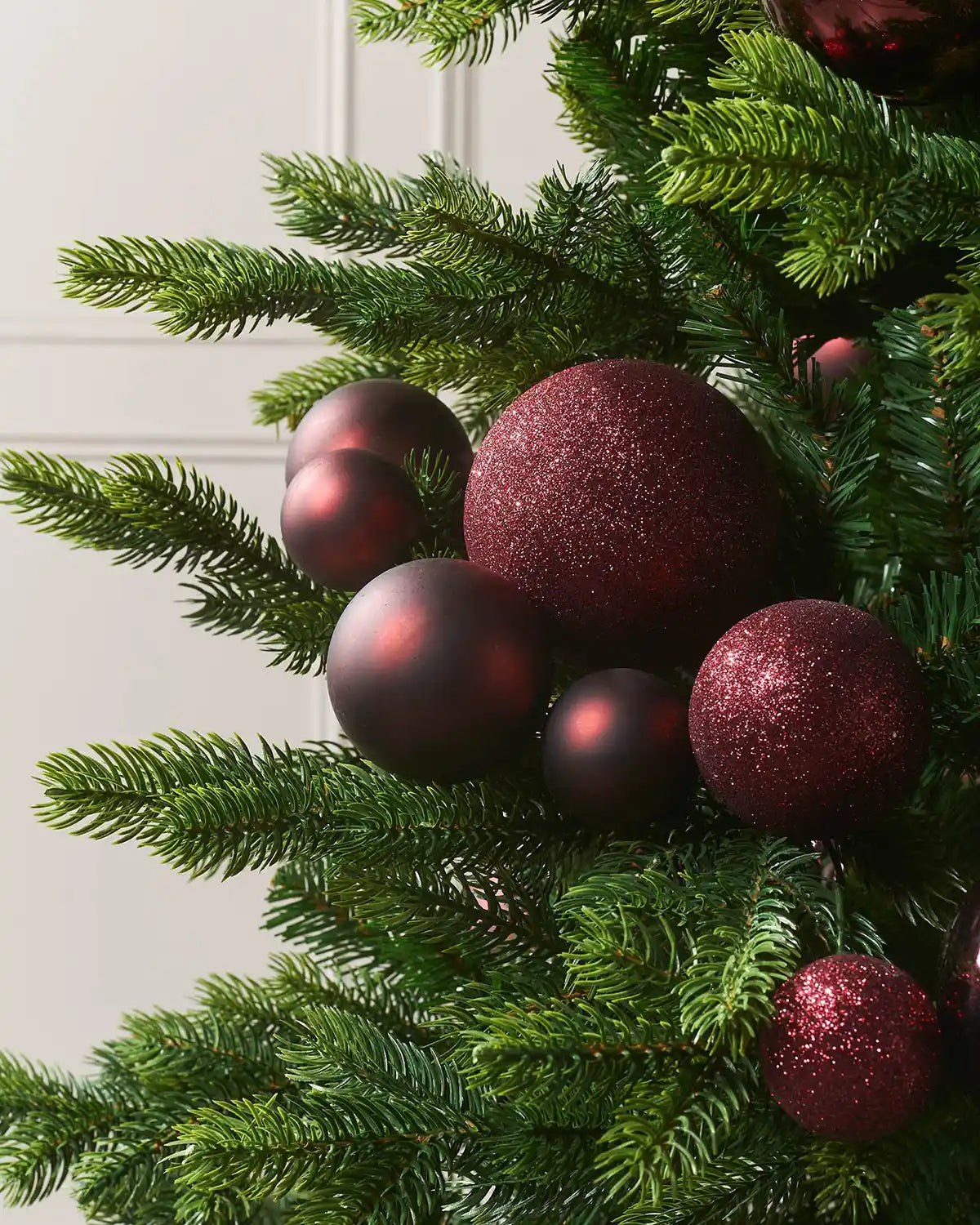 Decorative Christmas tree with burgundy bauble garland against a cream wall.
