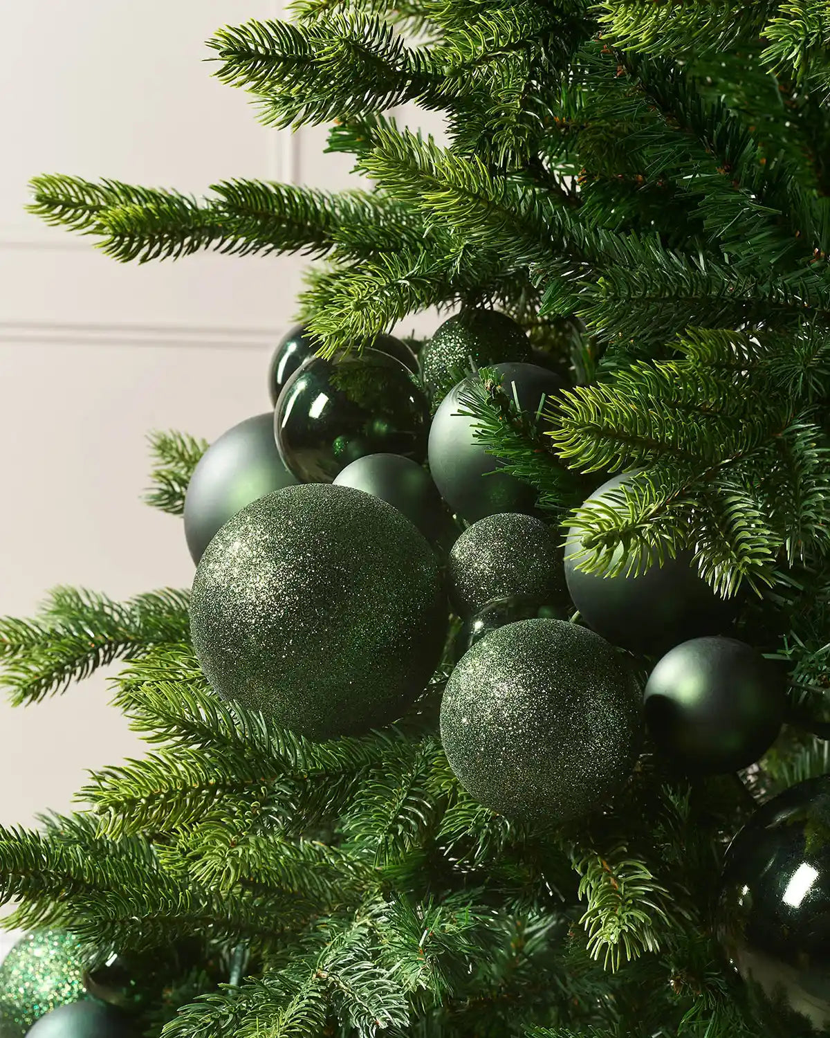 Decorative Christmas tree with sage green bauble garland against a cream wall.

