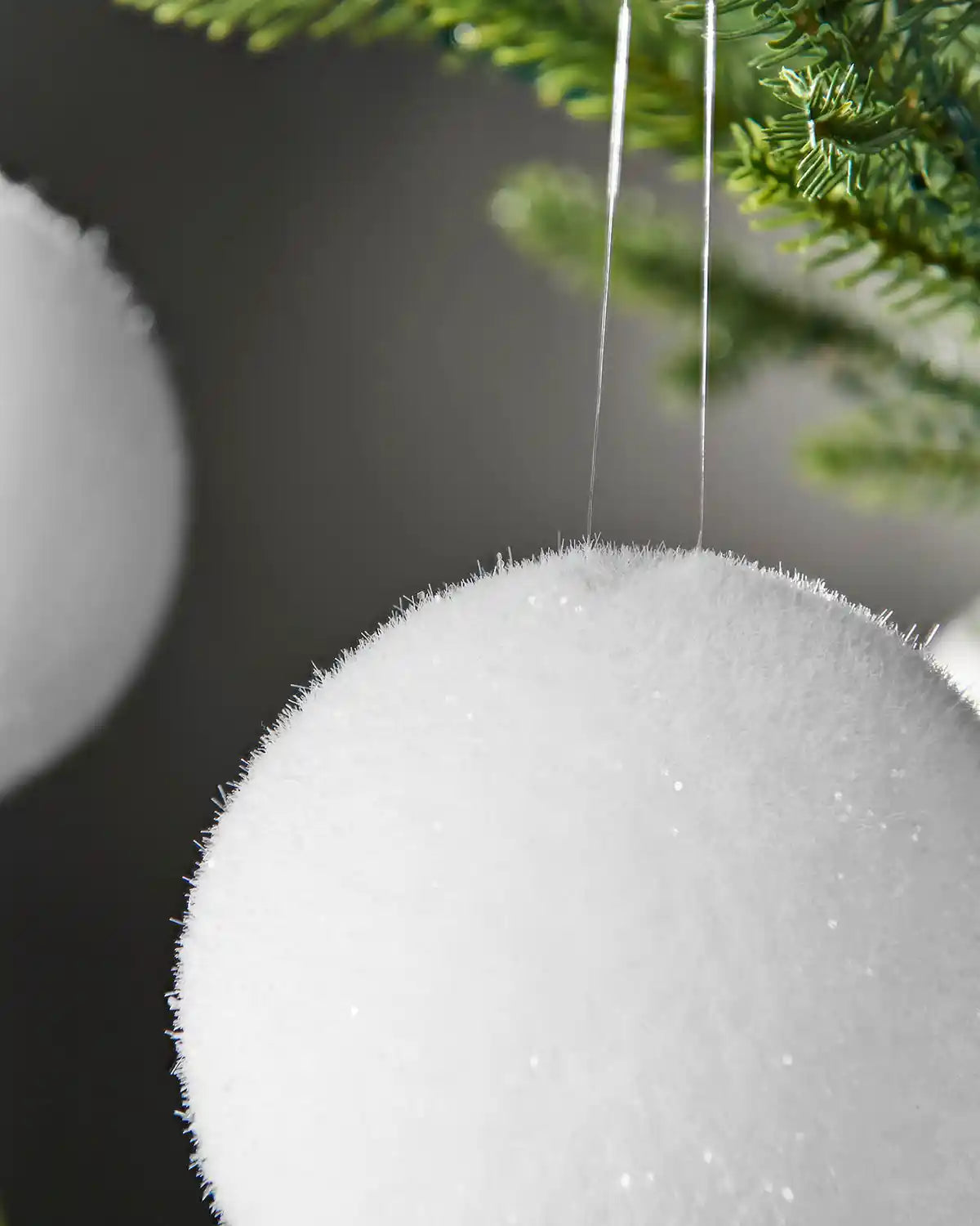 Close up a snowball bauble hanging on a Christmas tree branch against a Grey background