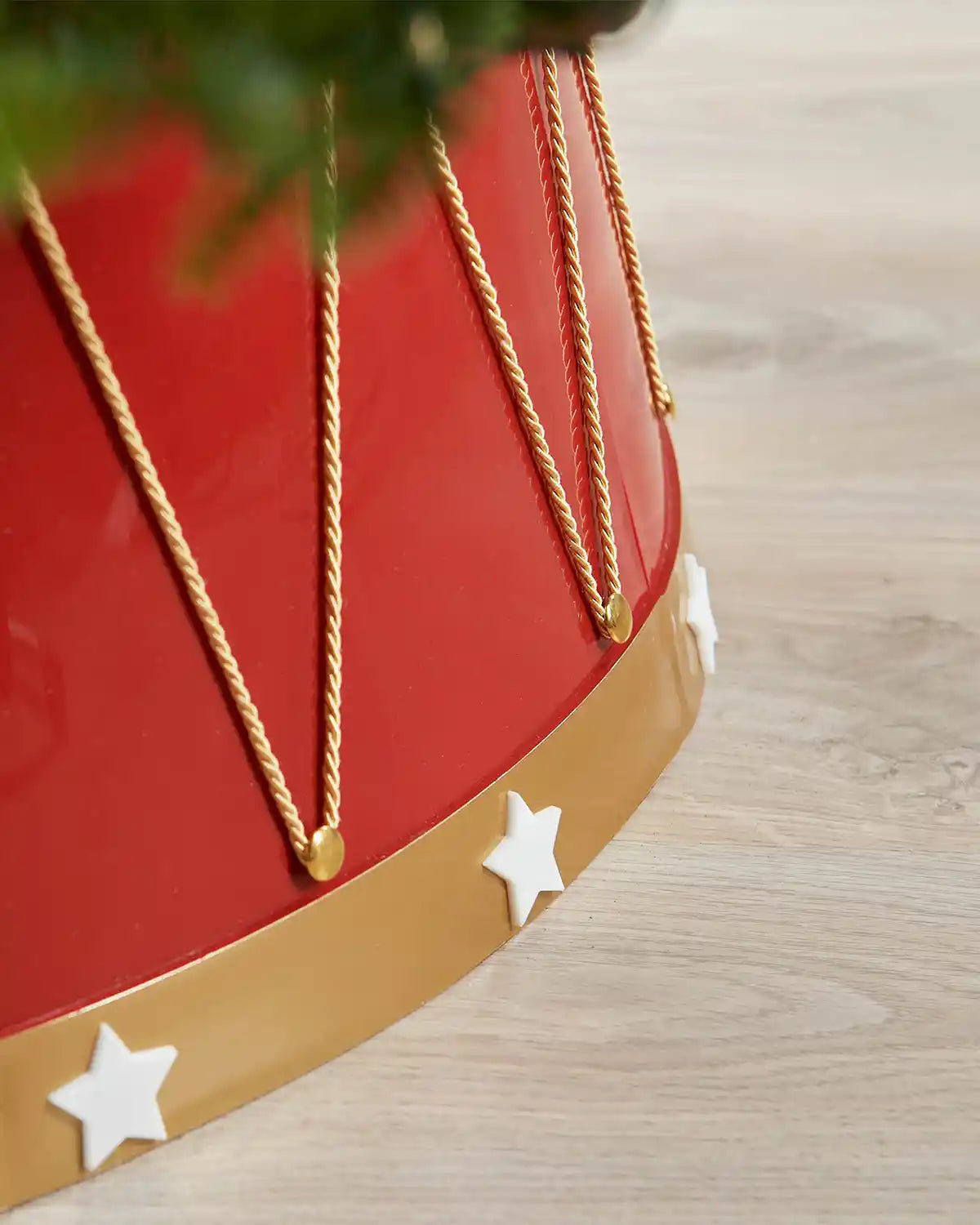 Close up of Red and gold Christmas tree stand with gold chains and white stars on a wooden floor.