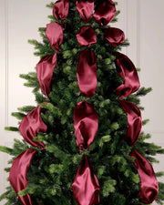 Decorative Christmas tree with burgundy satin ribbons against a white panelled wall.