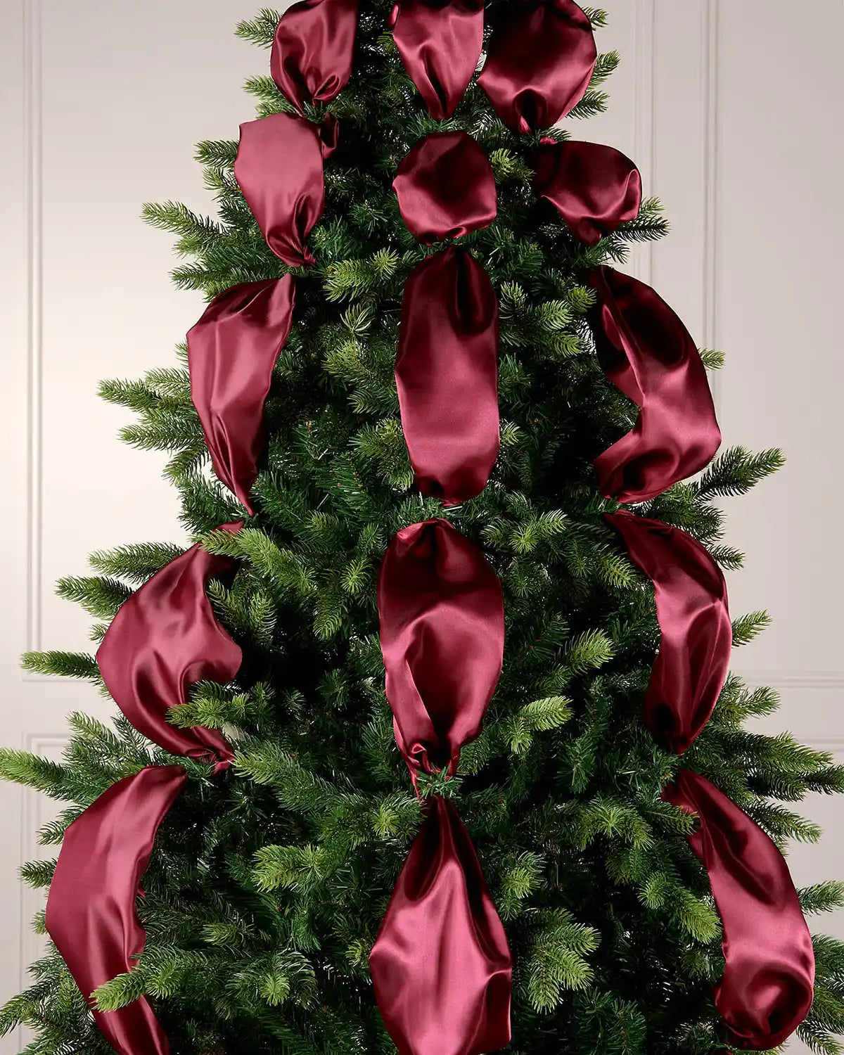 Decorative Christmas tree with burgundy satin ribbons against a white panelled wall.