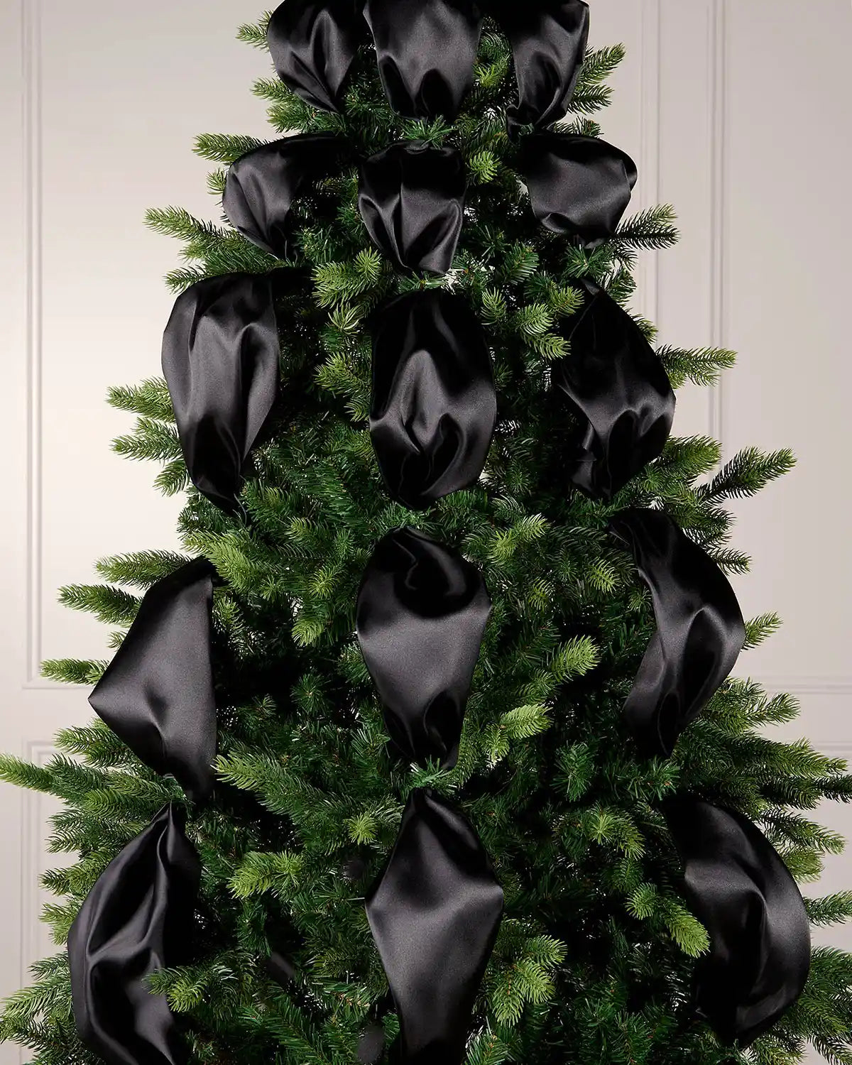 Decorative Christmas tree with black ribbons against a white wall