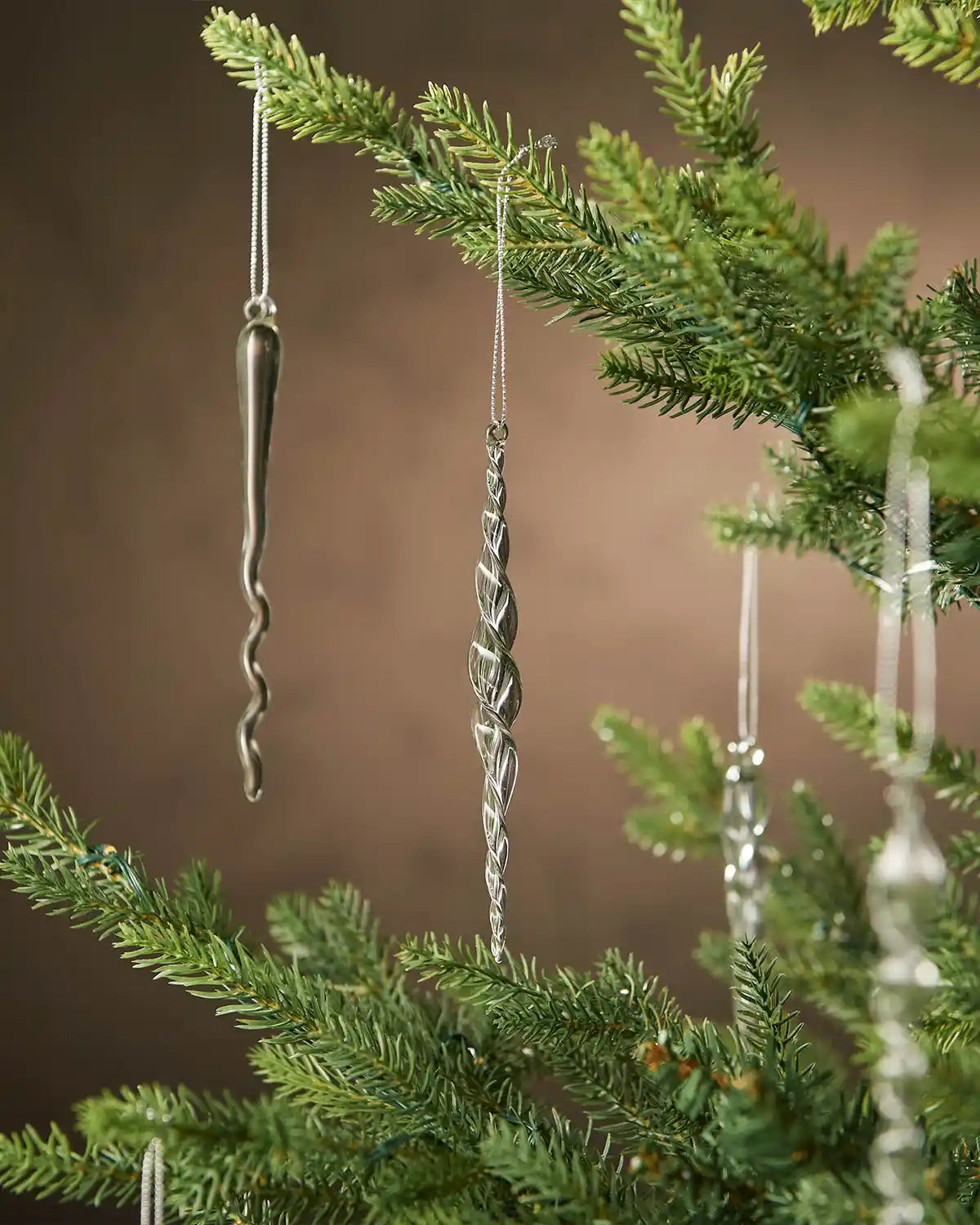 Decorative glass icicle ornaments hanging from a Christmas tree branch against a brown background
