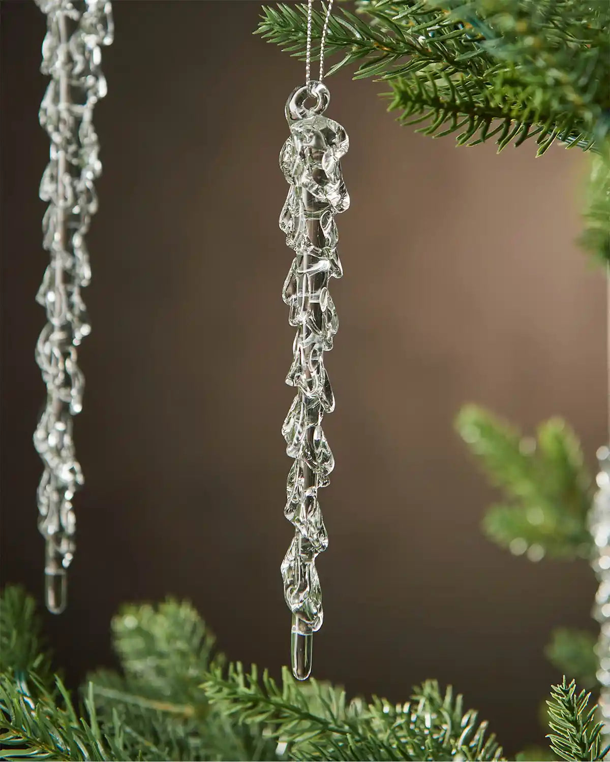 Two Crystal icicle ornament hanging on a Christmas tree with a blurred brown background