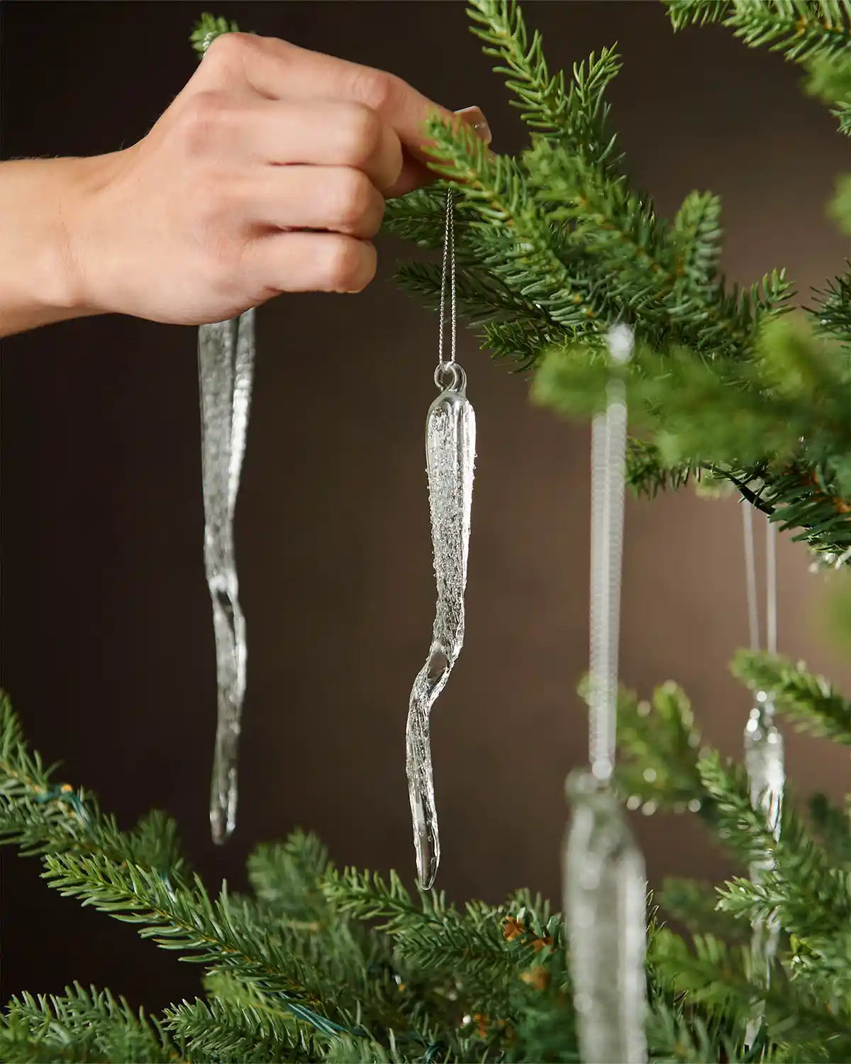 Hand holding a decorative frosted icicle ornaments hanging on a Christmas tree.