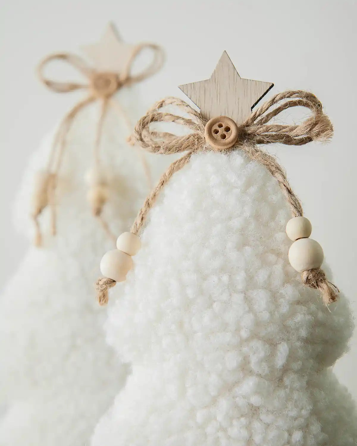 Close up of Two Sherpa mini trees with a wooden base on a table against a white wall