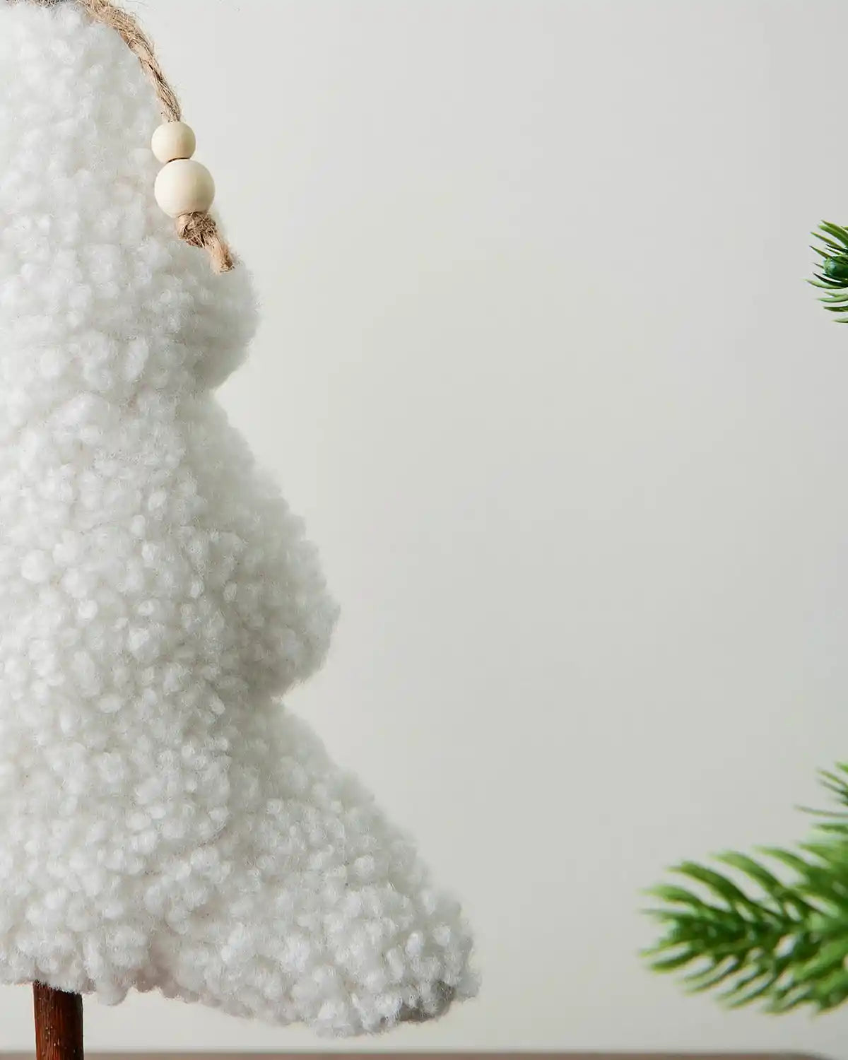 Decorative white sherpa tree with a bead ornament on a plain background