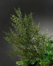 Green Cedar Christmas tree pick on a Christmas tree branch against a grey background