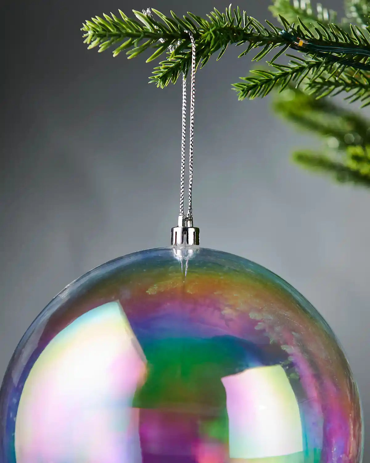 Iridescent Christmas ball ornament with silver thread hanging on a tree branch with a blurred background