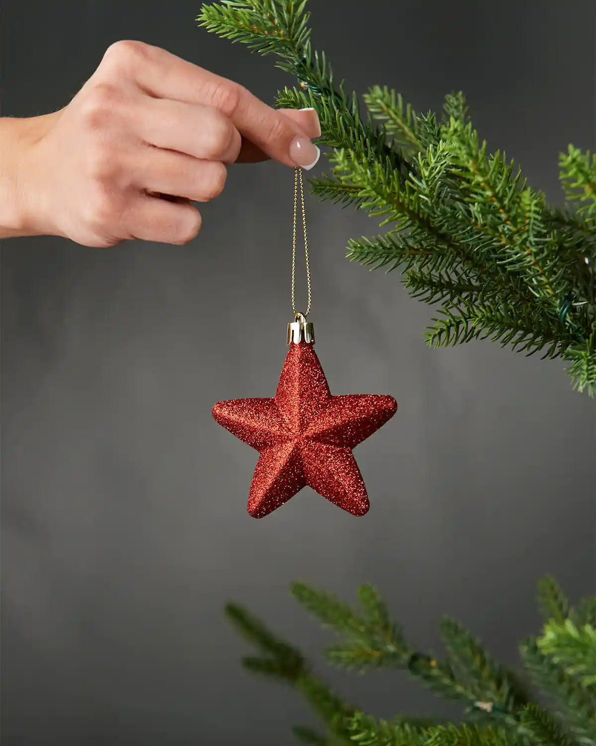 Hand holing glitter star shaped ornament against a Christmas tree on a grey background 