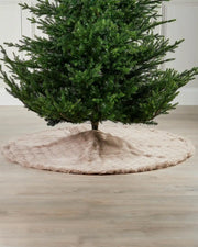 Christmas tree with a beige tree skirt on a wooden floor.