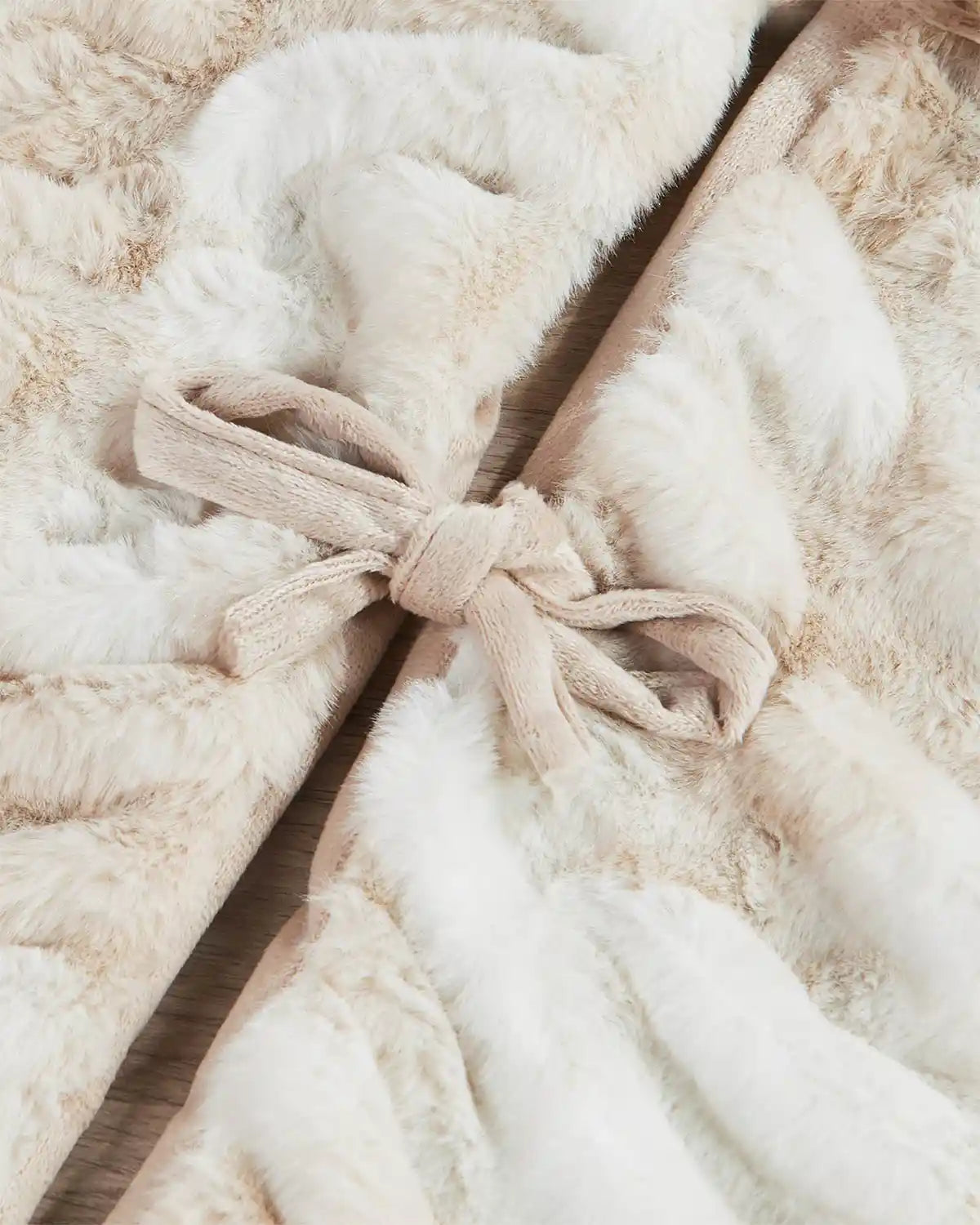 Close-up of a textured beige and white Christmas tree skirt with bows on a wooden floor