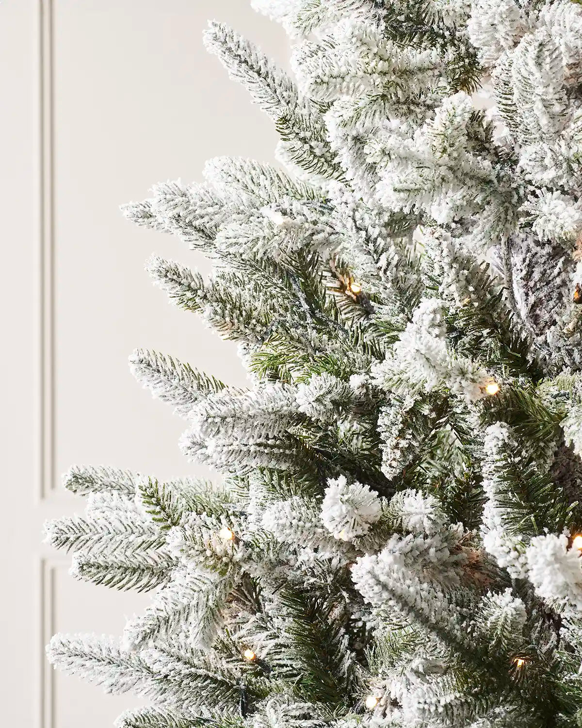 Snow flocked artificial Christmas tree with close up of white snow-like texture against a neutral background