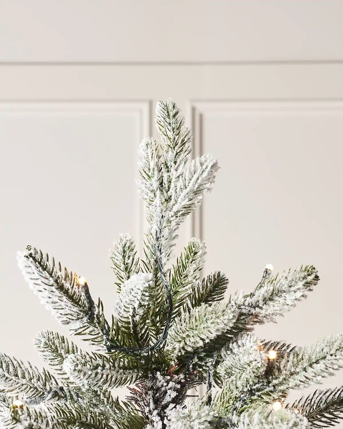Top of Frosted artificial Christmas tree with lights against a white wall