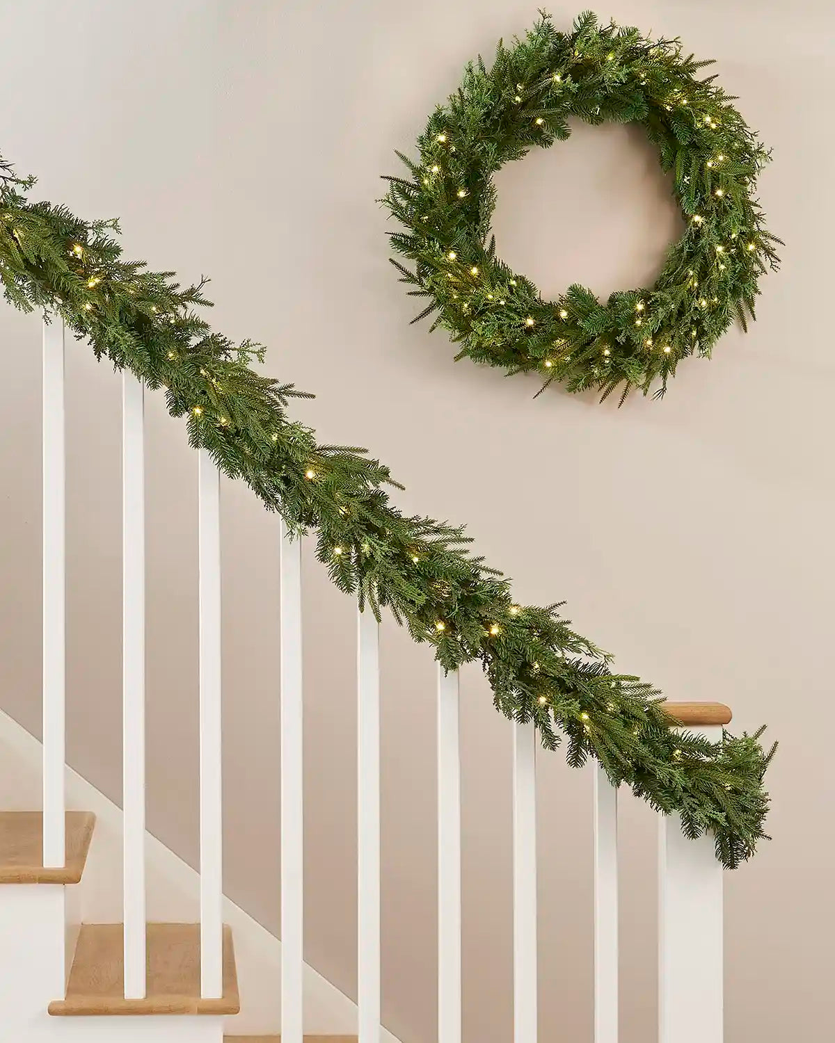 Green wreath and matching garland with warm white lights on a cream wall