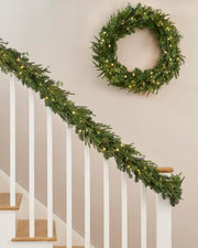 Green wreath and matching garland with warm white lights on a cream wall