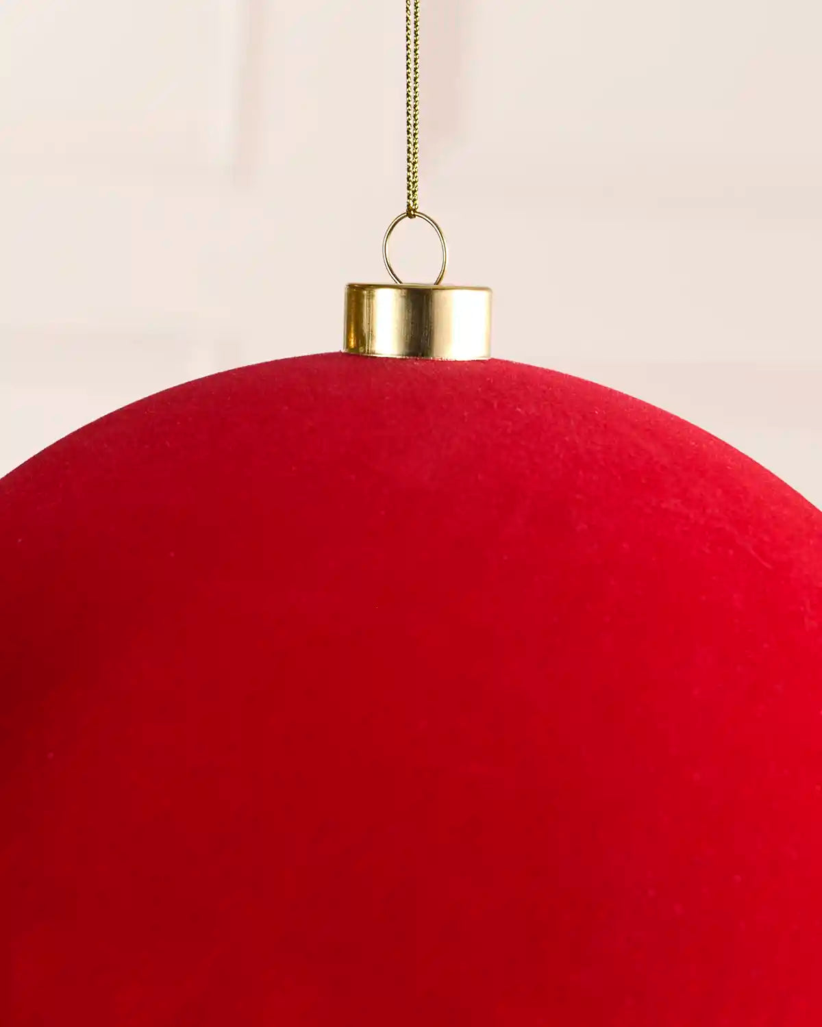A close-up of a large red spherical ornament with a metallic gold cap and a hanging chain against a light neutral background.