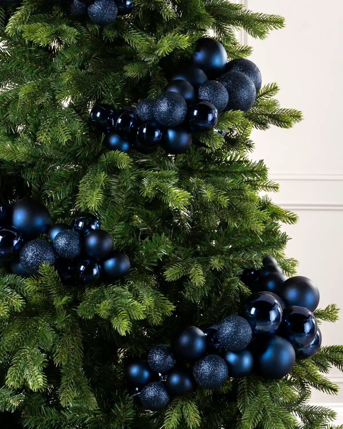 A close-up of a green Christmas tree decorated with glossy and glittery dark blue ornaments in various sizes.
