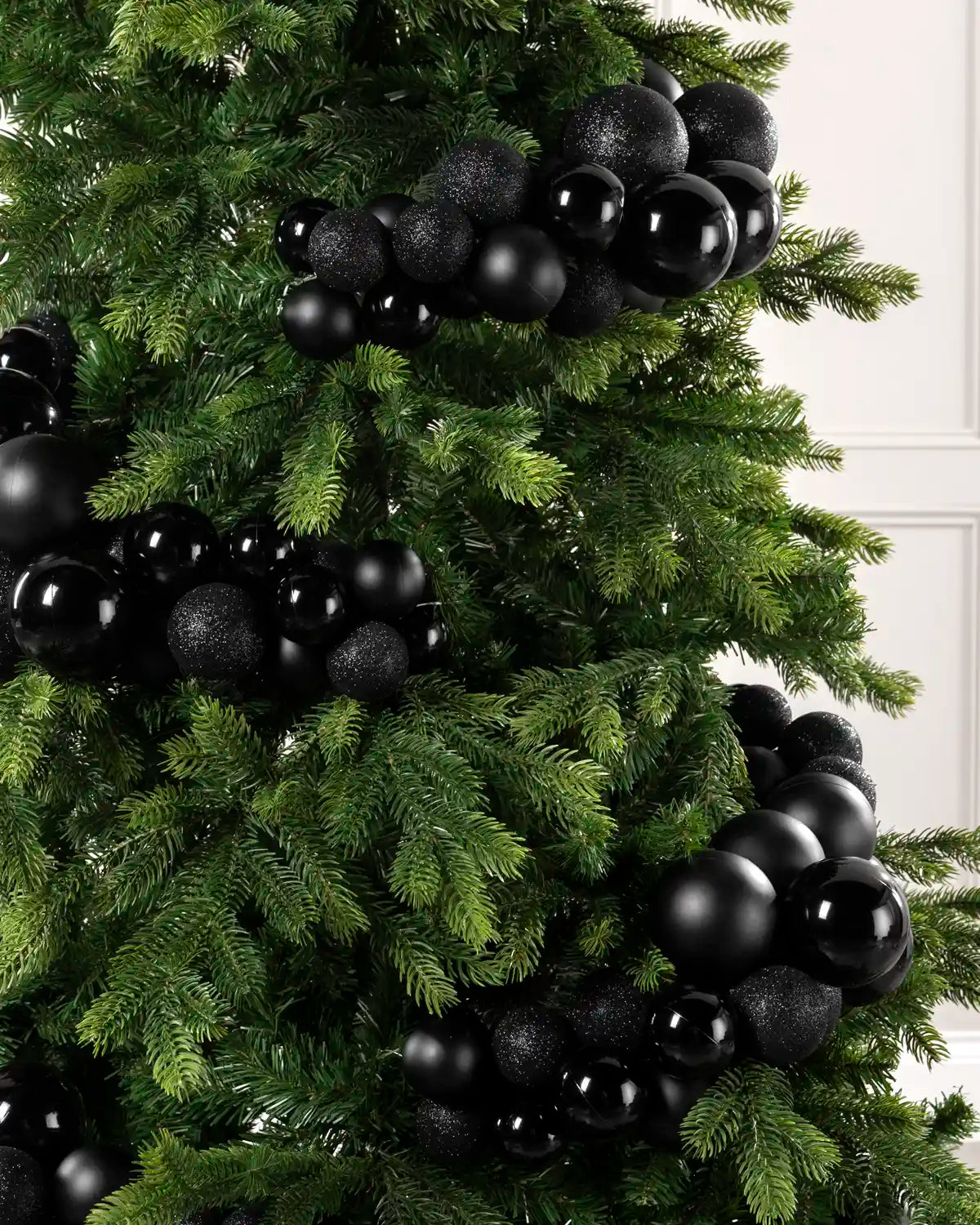 Black spherical Christmas tree ornaments, including both matte and textured glitter finishes, draped across a green artificial pine tree.