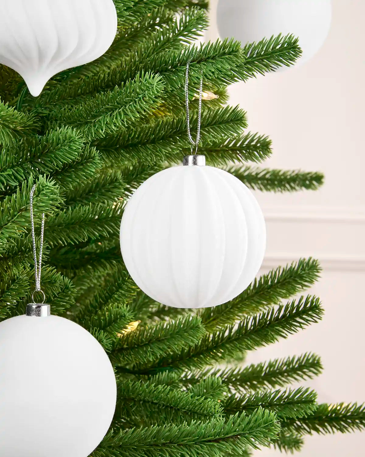 White ribbed spherical Christmas tree ornaments hanging on a green artificial tree, with silver hanging loops and caps.