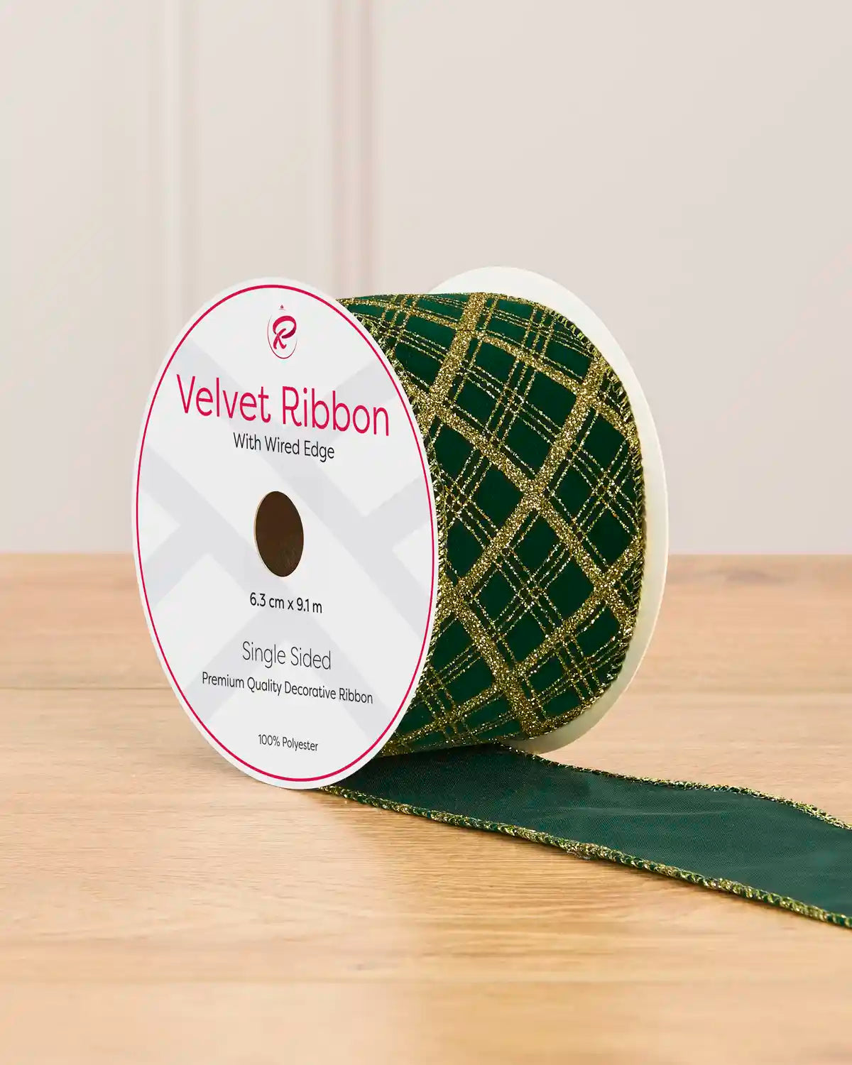 Green and gold tartan design ribbon with glitter gold lines on a cardboard roll placed on a wooden table against a light background