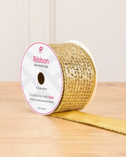 Gold ribbon with gold sequin squares on a cardboard roll placed on a wooden table against a light background