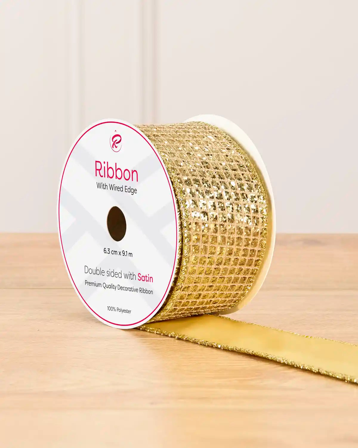 Gold ribbon with gold sequin squares on a cardboard roll placed on a wooden table against a light background