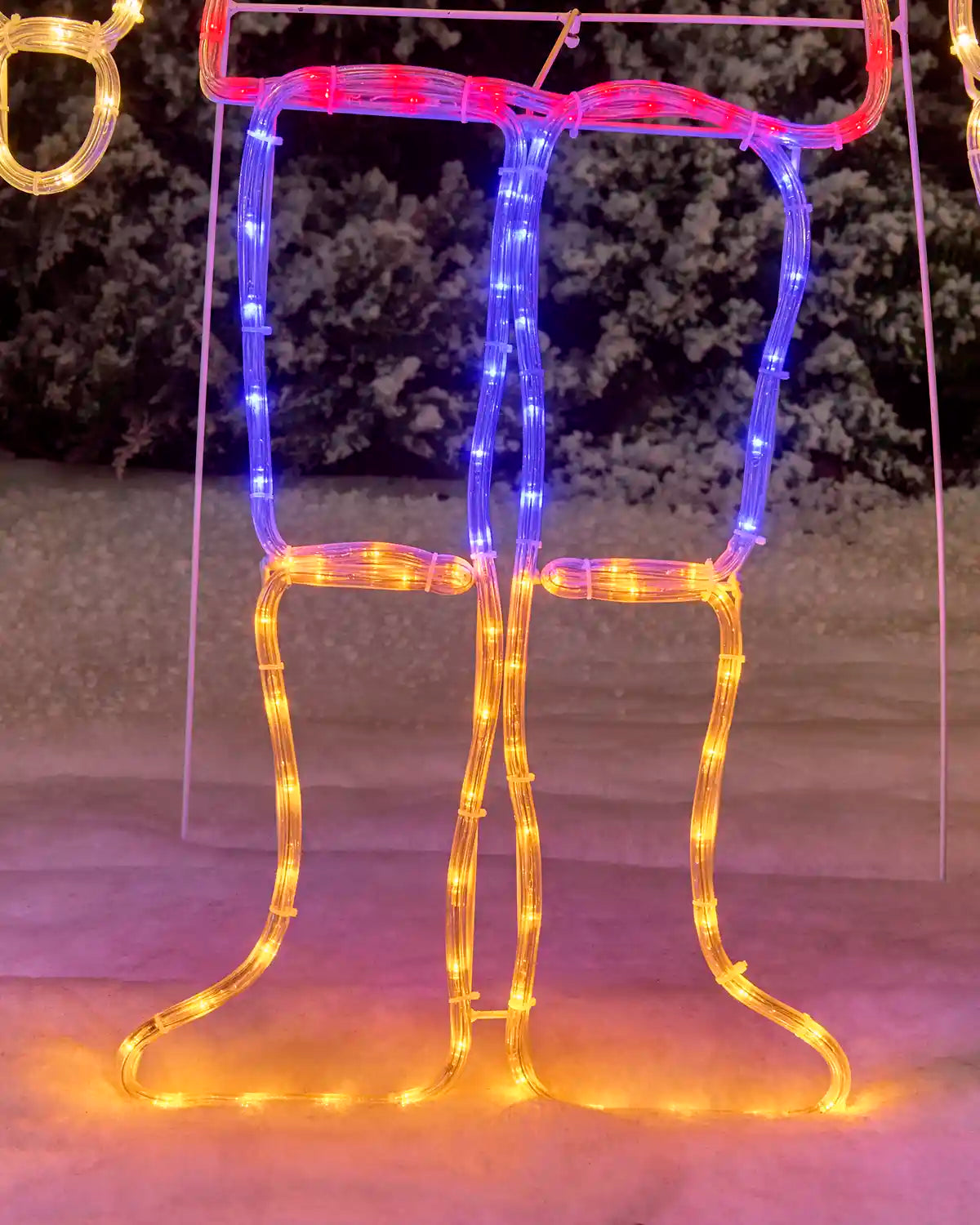 A festive holiday light decoration shaped like a pair of legs wearing a top, illuminated with blue LED lights on the upper portion and warm yellow LED lights on the lower legs, set outdoors at night.