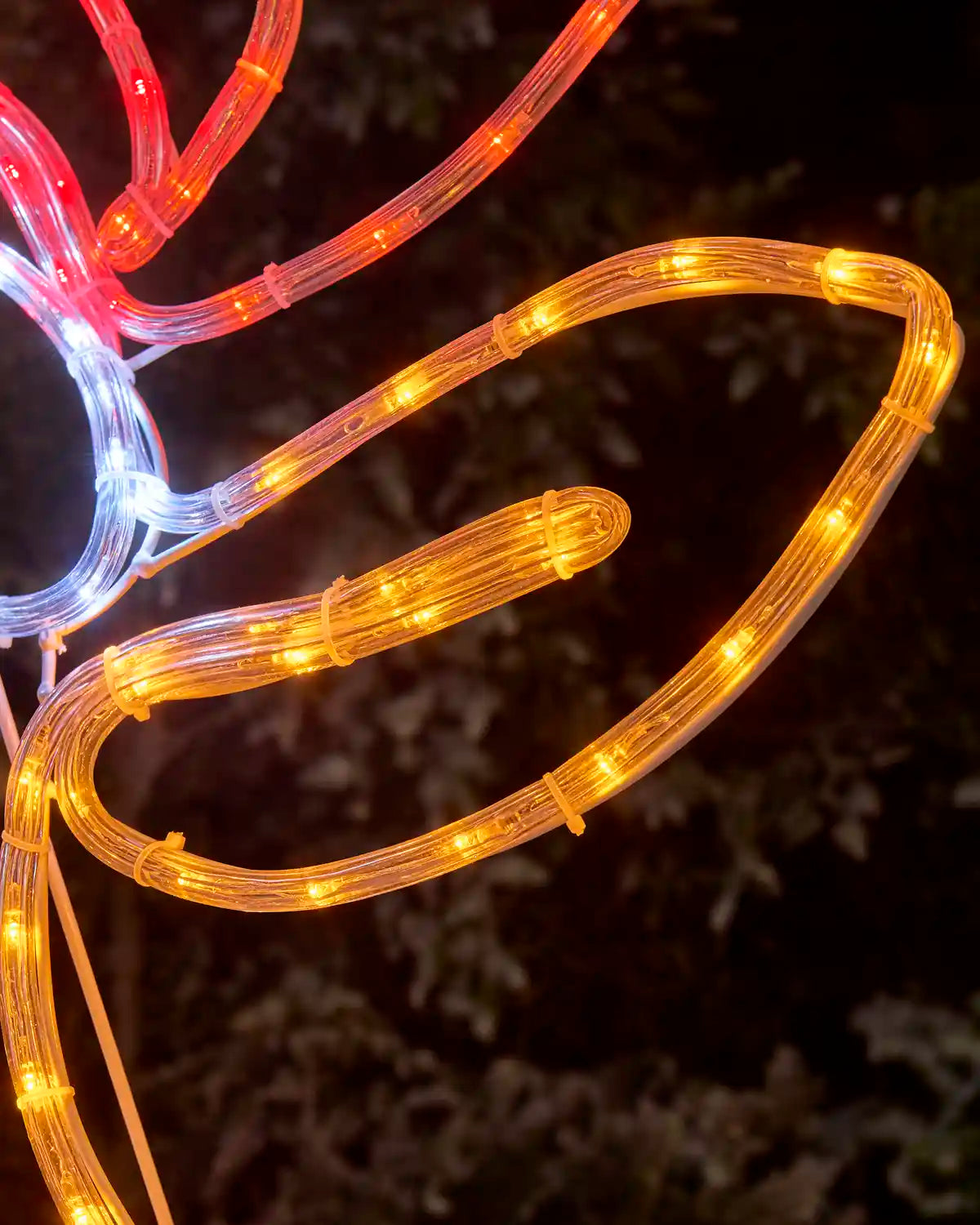 A close-up of a reindeers right ear in LED light decoration glowing in red, set against a dark, blurred outdoor background.