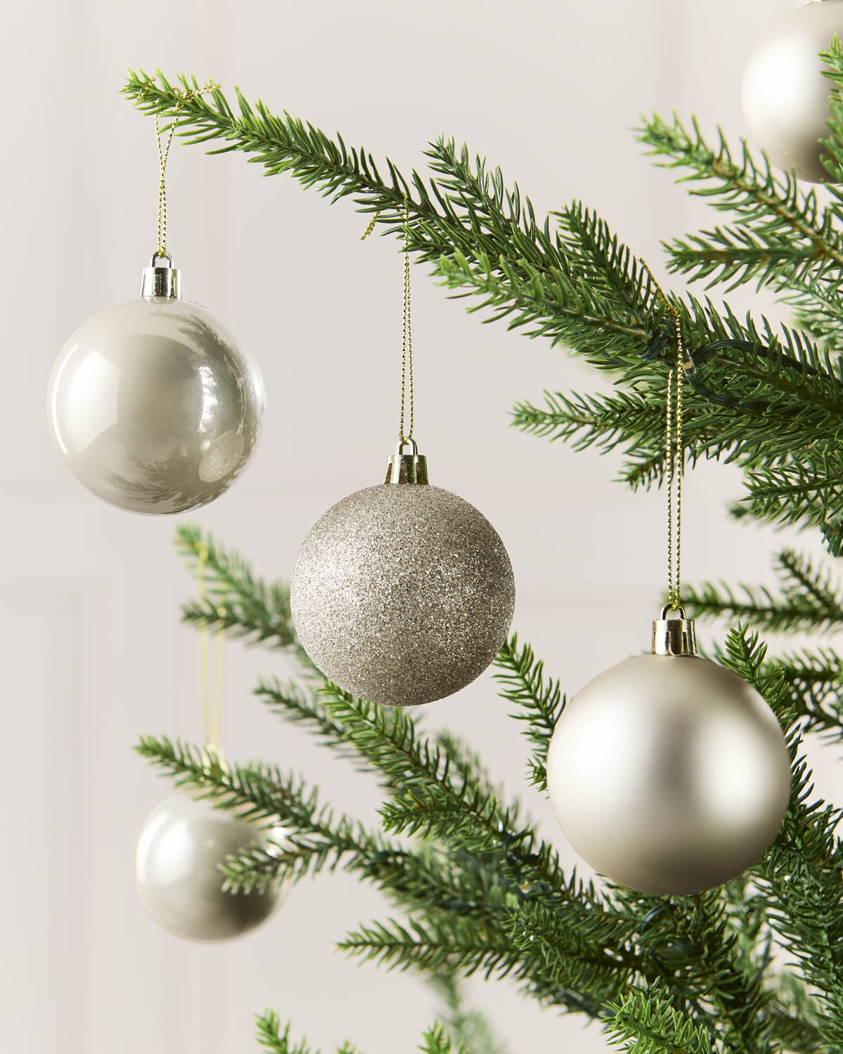 Four Latte coloured Christmas tree ornaments hanging from green pine branches against a soft light background.
