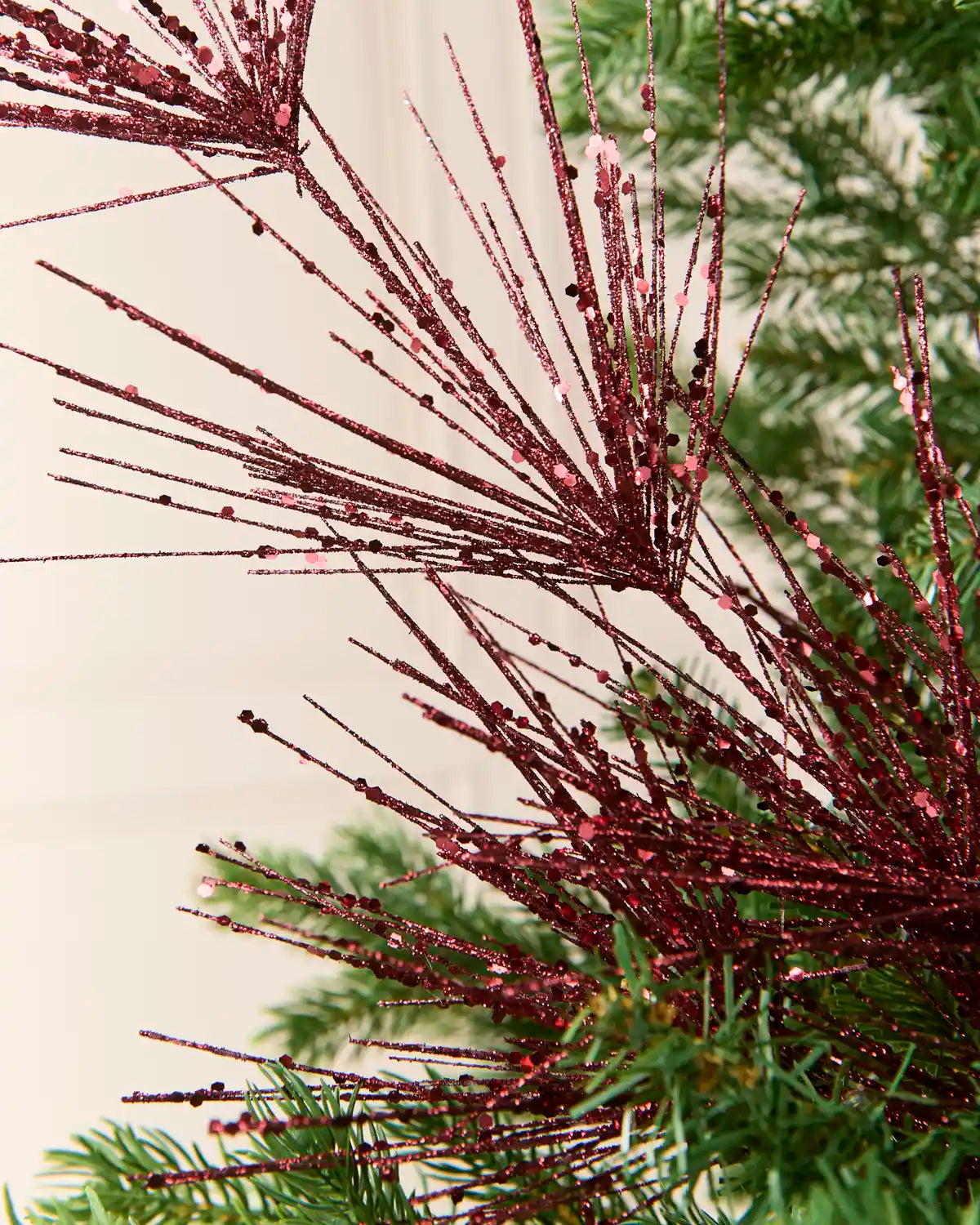 Close-up view of Burgundy  glitter firework branches extending from a central stem among the green branches of a Christmas tree