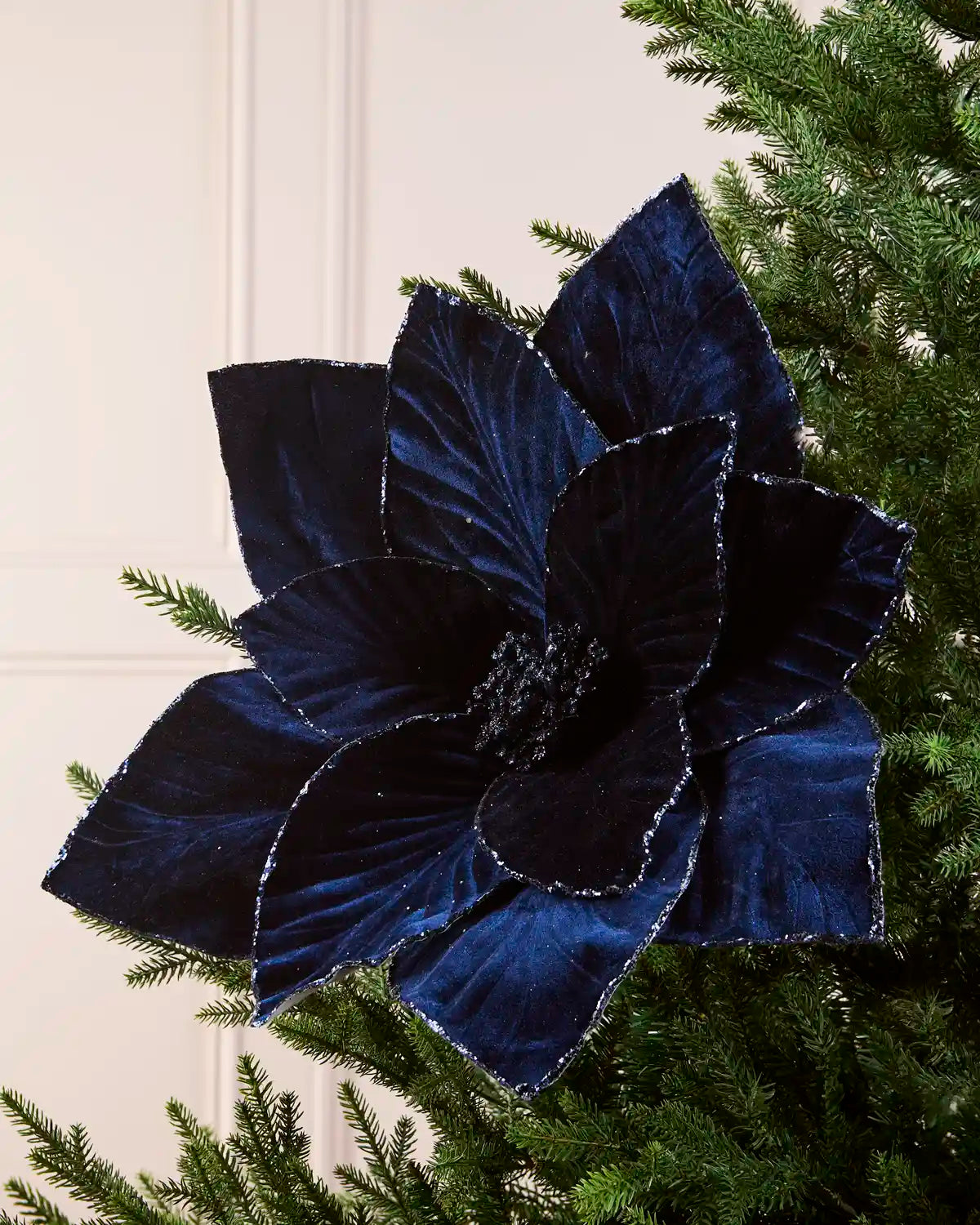 Navy oversized velvet artificial poinsettia displayed on a Christmas tree, featuring layered velvet petals with glittered edges and a sparkling center
