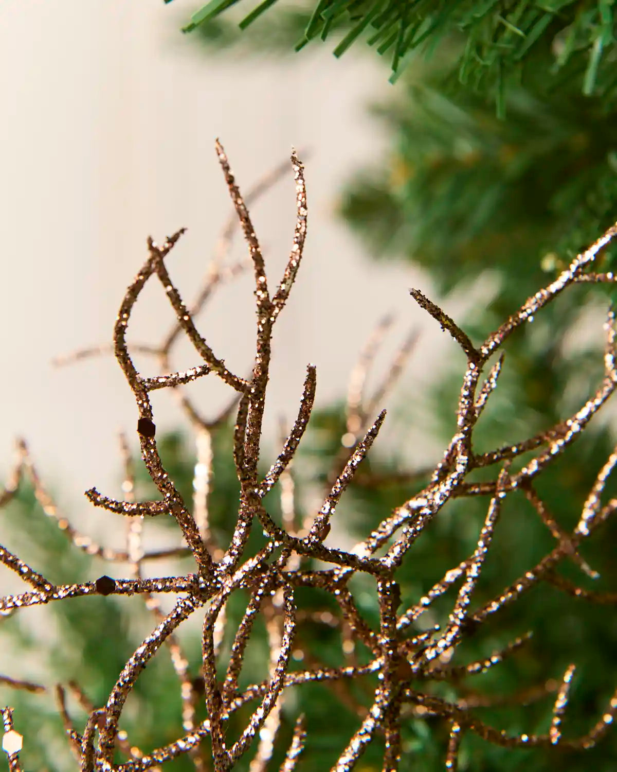 Close-up of a decorative branch-like ornament with a glittery espresso colour, shown against a soft-focus background with green pine needles.