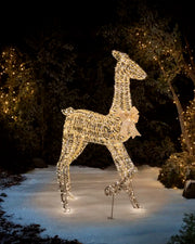 Warm white LED gold doe silhouette with a gold glitter bow on its neck against a dark garden setting on snowy grass