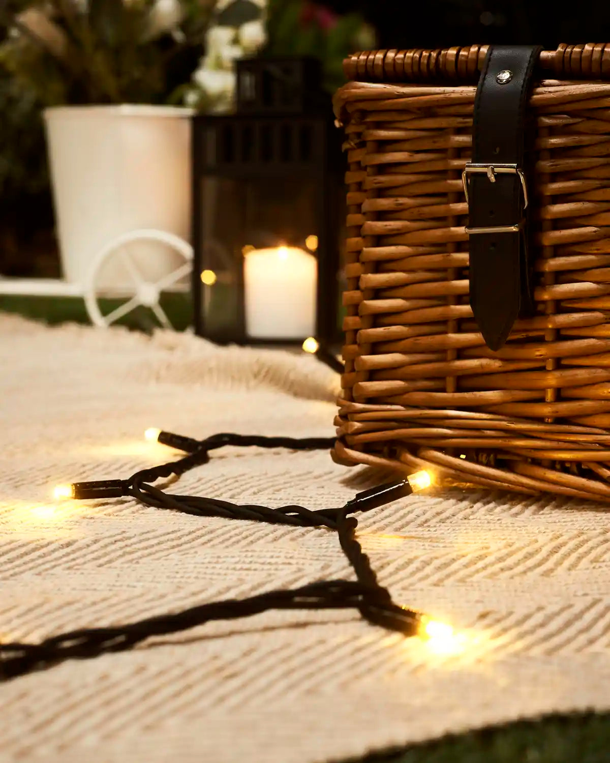 Warm white LED string light on a white cloth with a wicker basket and a blurry garden set background. 