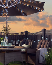 Warm white and ice white sting lights wrapped around an outdoor umbrella with a sun set background and outdoor furniture