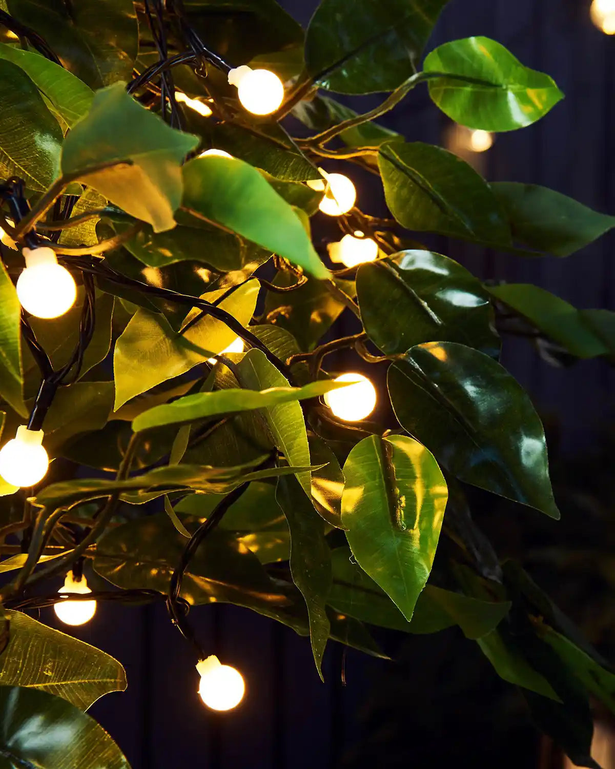 Close up of Warm white berry lights on an artificial garden tree against a dark blue fence 